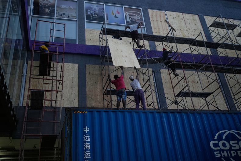 Trabajadores cubren ventanas de un comercio antes de la llegada del huracán Melissa en Kingston, Jamaica, el domingo 26 de octubre de 2025. (AP Foto/Matias Delacroix)