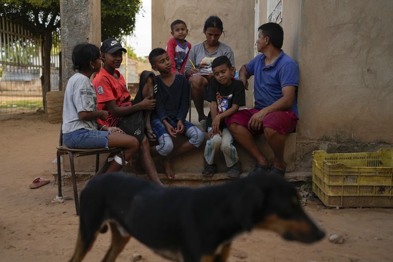 José Romero, a la derecha, su esposa Yoselin Pérez y sus cinco hijos, que regresaron a Venezuela desde México después de abandonar los planes de llegar a Estados Unidos en medio de la represión migratoria del presidente Donald Trump, se sientan en su porche en Maracaibo, Venezuela, el lunes 16 de junio de 2025. (AP Foto/Matias Delacroix)