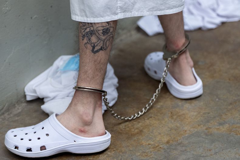 Un prisionero con un tatuaje en la pierna y esposas permanece de pie mientras la secretaria de Seguridad Nacional de Estados Unidos, Kristi Noem, recorre el Centro de Confinamiento del Terrorismo el miércoles 26 de marzo de 2025, en Tecoluca, El Salvador. (AP Foto/Alex Brandon)