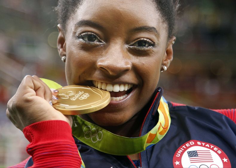 La gimnasta estadounidense Simone Biles muerde su medalla de oro tras ganar la medalla de oro en el concurso completo de los Juegos Olímpicos de Río de Janeiro 2016, el 11 de agosto de 2016. (AP Foto/Dmitri Lovetsky)