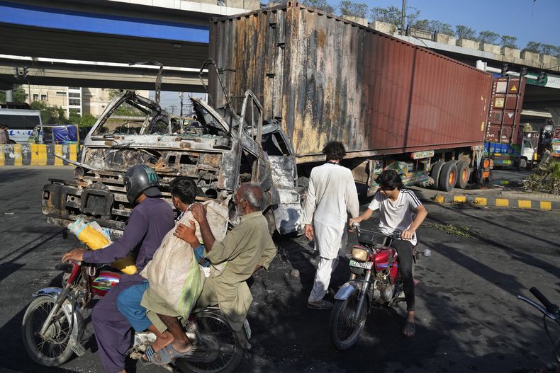 Varias personas en motocicleta pasan por delante de un camión calcinado durante enfrentamientos entre la policía y partidarios del ex primer ministro Imran Khan, en Lahore, Pakistán, el 11 de mayo de 2023. (AP Foto/K.M. Chaudary)