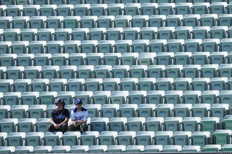 Aficionados de los Dodgers de Los Ángeles observan desde asientos vacíos mientras se protegen del sol y el calor antes del primer juego de una serie divisional de los playoffs de la Liga Nacional de béisbol contra los Bravos de Atlanta, el 3 de octubre de 2026, en Los Ángeles. (Foto AP/Jae C. Hong)