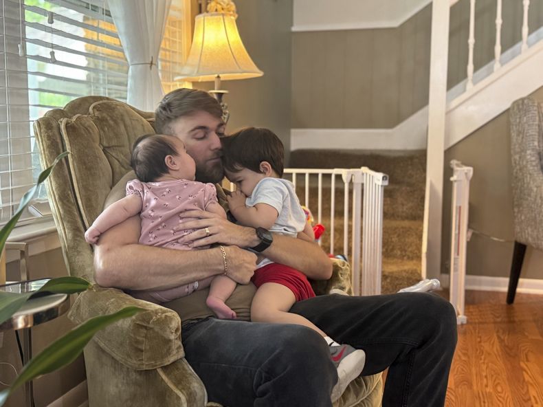 El veterano de marines Adrian Clouatre abraza a su hija de 3 meses, Lyn y a su hijo de casi dos años, Noah, en su casa en Baton Rouge, Luisiana, el martes 17 de junio de 2025. (AP Foto/Stephen Smith)