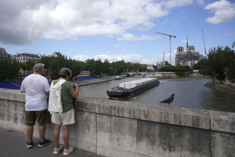 Dos turistas observan la Catedral de Notre Dame desde un puente sobre el Río Sena, el jueves 4 de julio de 2024, en París (AP Foto/Thibault Camus)