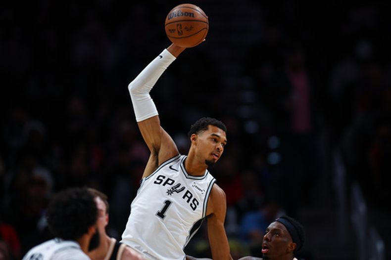 El alero de los Spurs de San Antonio, Victor Wembanyama (1), atrapa un pase por encima del alero de los Hawks de Atlanta, Onyeka Okongwu, a la derecha, durante la primera mitad de un juego de baloncesto de la NBA, el viernes 19 de diciembre de 2025, en Atlanta. (AP Photo/Colin Hubbard)