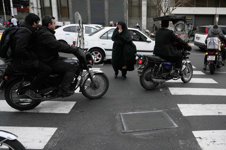Una mujer cruza una calle mientras las motocicletas pasan en Teherán, Irán, el martes 24 de febrero de 2026. (AP Foto/Vahid Salemi)