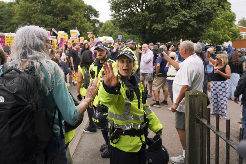 Un policía reacciona mientras manifestantes sostienen pancartas y estandartes al terminar una protesta fuera del hotel Bell en Epping, cerca de Londres, el domingo 27 de julio de 2025. (AP Foto/Alberto Pezzali)