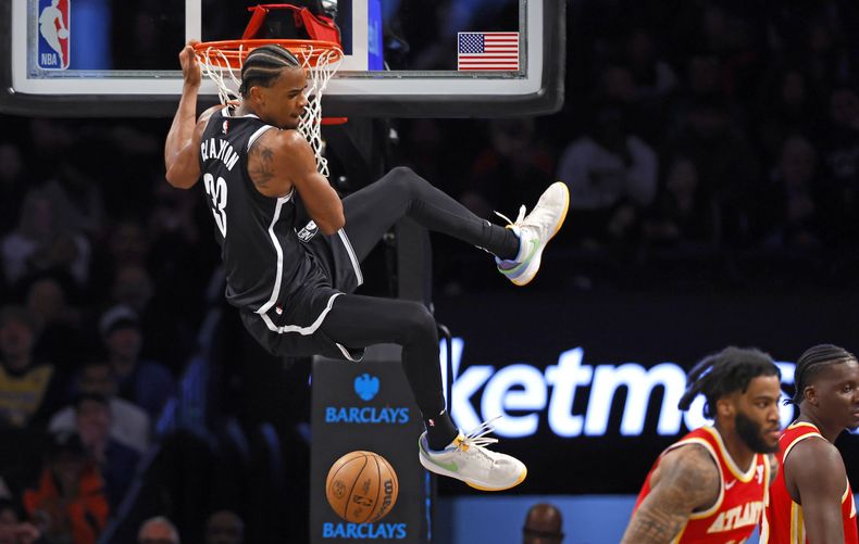 Nic Claxton, pívot de los Nets de Brooklyn, se cuelga del aro tras realizar una volcada ante los Hawks de Atlanta, el sábado 2 de marzo de 2024 (AP Foto/Noah K. Murray)