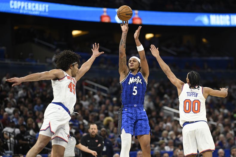 El escolta del Magic de Orlando Paolo Banchero (5) lanza entre el centro de los Knicks de Nueva York Jericho Sims (45) y el alero Jacob Toppin (00) durante la segunda mitad del juego de baloncesto de la NBA, el miércoles 14 de febrero de 2024, en Orlando, Florida. (AP Foto/Phelan M. Ebenhack)