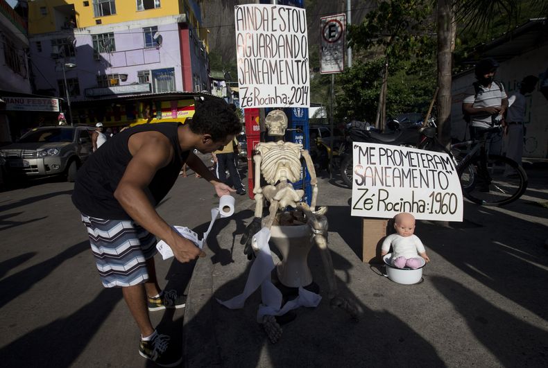 Un hombre obsequia papel sanitario a un esqueleto durante una manifestaci&oacute;n en la favela de Rocinha, a favor del tratamiento de aguas de alba&ntilde;al en ese barrio pobre ubicado en R&iacute;o de Janeiro, Brasil, el s&aacute;bado 22 de febrero de