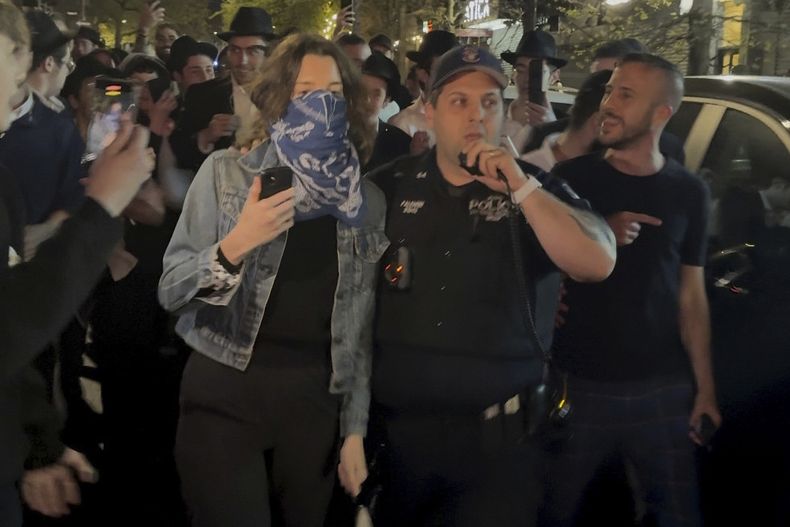 Esta imagen tomada de un video muestra a una mujer y a un agente de la policía mientras son perseguidos por una multitud de judíos ortodoxos en el vecindario de Crown Heights en Brooklyn, Nueva York, el jueves 24 de abril de 2025. (AP Foto)