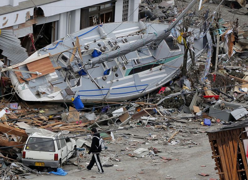 ARCHIVO-Un hombre pasa junto a un yate varado en una zona azotada por un tsunami en Ofunato, en la prefectura de Iwate, Japón, el 15 de marzo de 2011, cuatro días después del desastre. (AP Foto/Itsuo Inouye, archivo)