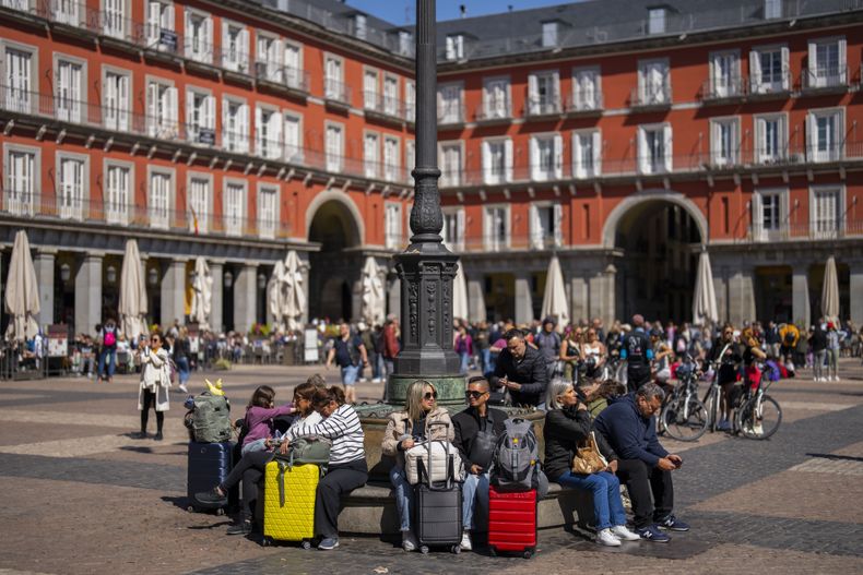 En esta imagen de archivo, turistas esperan sentados con sus maletas en un banco de la Plaza Mayor, en el centro de Madrid, el 29 de abril de 2024. (AP Foto/Bernat Armangue, archivo)