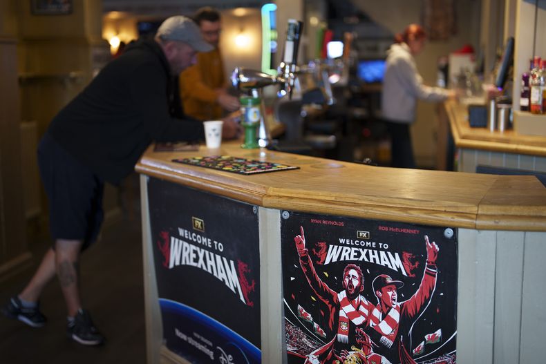 Un cartel que anuncia el documental de televisión Welcome to Wrexham adorna el bar del Turf Pub junto al hipódromo del Wrexham Football Club en Wrexham, Gales, el lunes 7 de octubre de 2024. (Foto AP/Jon Super)