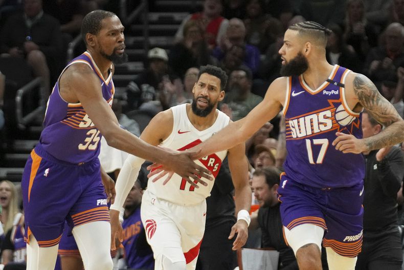 Kevin Durant (35), de los Suns de Phoenix, choca palmas con Cody Martin (17) después de acertar un triple frente a Garrett Temple, centro, de los Raptors de Toronto, durante la segunda mitad del juego de baloncesto de la NBA, el lunes 17 de marzo de 2025, en Phoenix. (AP Foto/Darryl Webb)