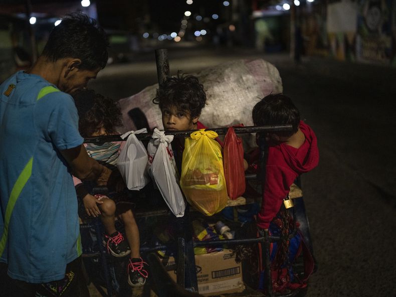 Los hijos de Germán Mosquera -- Jodana (izquierda), Jordar (centro) y Liam (sentado en su carro de reciclaje) -- acompañan a su padre durante su jornada recogiendo cartón y metal usado para vender, en el centro de Guayaquil, Ecuador, el 29 de septiembre de 2023. Mosquera dijo que gana entre tres y cinco dólares al día. (AP Foto/Rodrigo Abd)