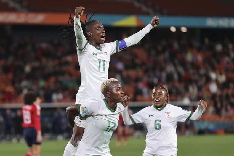 La jugadora de Zambia Racheal Kundananji lleva a su compañera Barbra Banda a la espalda, mientras Mary Wilombe, a la derecha, corre para celebrar el tercer gol del equipo en un partido del Grupo C entre Costa Rica y Zambia en Hamilton, Nueva Zelanda, el lunes 31 de julio de 2023. (AP Foto/Juan Mendez)