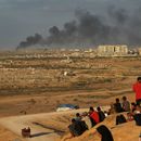 Palestinos desplazados observan cómo se eleva el humo por los ataques del ejército israelí mientras se reúnen en la carretera costera cerca de Wadi Gaza, en el centro de la Franja de Gaza, el jueves 9 de octubre de 2025. (AP Foto/Abdel Kareem Hana)