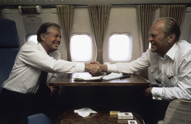 ARCHIVO - El expresidente Jimmy Carter estrecha la mano del expresidente Gerald Ford abordo del avión presidencial el 10 de octubre de 1981, entre El Cairo y España. (AP Foto/Dirck Halstead, archivo)