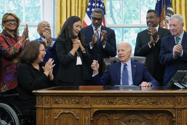 El presidente Joe Biden, junto a líderes de derechos civiles, miembros de la comunidad y funcionarios electos, habla tras entregar a la secretaria del Interior, Deb Haaland, cuarta de izquierda derecha, la pluma que uso para firmar la proclamación para designar como monumento nacional el sitio de los disturbios raciales de 1908 en Springfield, en la Oficina Oval de la Casa Blanca en Washington, el viernes 16 de agosto de 2024. (AP Foto/Susan Walsh)