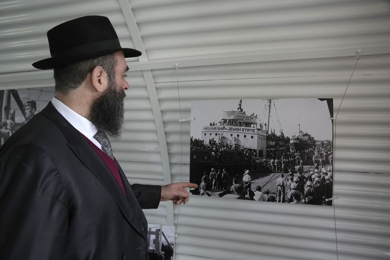 El rabino Arie Zeev Raskin mira una exhibición fotográfica en una réplica de las barracas de un campo de internamiento para refugiados judíos de Europa que trataban de llegar al territorio palestino tras la Segunda Guerra Mundial, en la ceremonia para conmemorar el 76to aniversario del cierre de una docena de dichos sitios, en el Campamento de la Guardia Nacional chipriota que albergó un hospital militar británico en Nicosia, el martes 18 de febrero de 2025. (AP Photo/Petros Karadjias)
