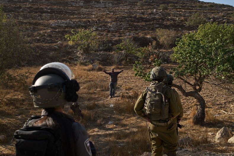 Un colono israelí hace gestos mientras soldados israelíes bloquean el acceso a palestinos a una zona para cosechar aceitunas en el poblado cisjordano de Sair, cerca de Hebrón, el jueves 23 de octubre de 2025. (AP Foto/Leo Correa)