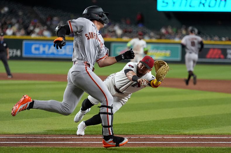 El primera base de los Diamondbacks de Arizona, Ildemaro Vargas, derecha, se lanza para tocar a Jung Hoo Lee, izquierda, de los Gigantes de San Francisco, quien fue declarado fuera de la línea durante la novena entrada del juego de béisbol de Grandes Ligas, el lunes 29 de junio de 2026, en Phoenix. (AP Foto/Ross D. Franklin)