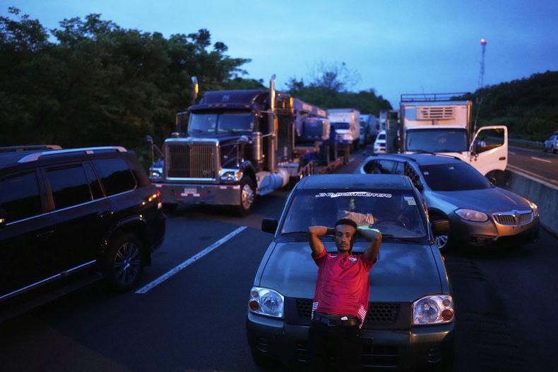 Un conductor se apoya en su vehículo mientras el tráfico se congestiona en la Carretera Panamericana, bloqueada por manifestantes antigubernamentales que se oponen a las reformas de la seguridad social y a un memorando entre Panamá y Estados Unidos sobre el Canal de Panamá, en El Piro, Panamá, el miércoles 14 de mayo de 2025. (Foto AP/Matías Delacroix)