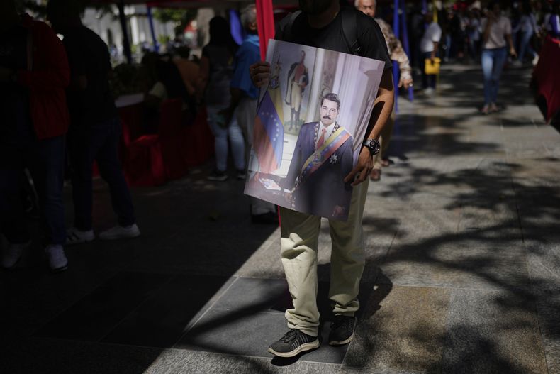 Un hombre llega con una foto del presidente venezolano Nicolás Maduro para unirse a la milicia civil durante una campaña nacional de alistamiento en un museo militar en Caracas, Venezuela, el viernes 29 de agosto de 2025. (Foto AP/Ariana Cubillos)