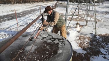 Walt Traywick usa un hacha para romper agua congelada en un tanque mientras trabaja en su granja, el miércoles 19 de febrero de 2025, en Luther, Oklahoma. (AP Foto/Joshua A. Bickel)