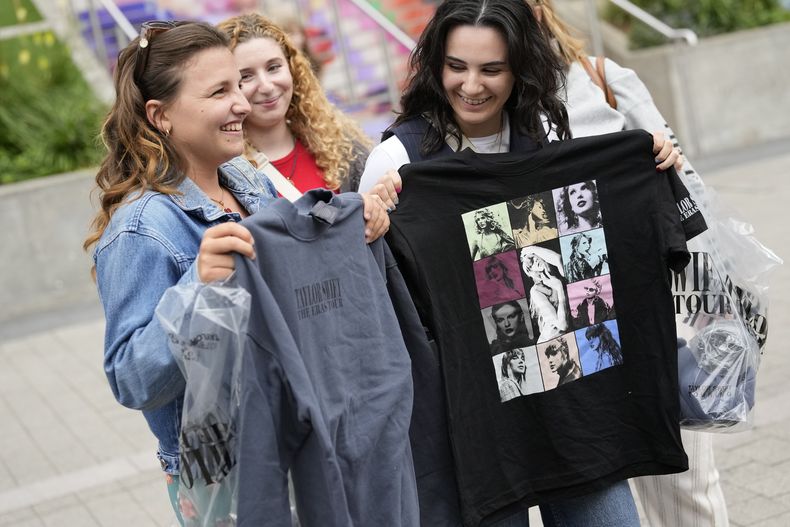 Francesca Abela, derecha, y Kylie Micallef, ambas de Malta, muestran sus productos de Taylor Swift que acaban de comprar en el estadio de Wembley en Londres, el miércoles 14 de agosto de 2024, antes de asistir al concierto de Swift en Wembley el jueves. (Foto AP/Alastair Grant)