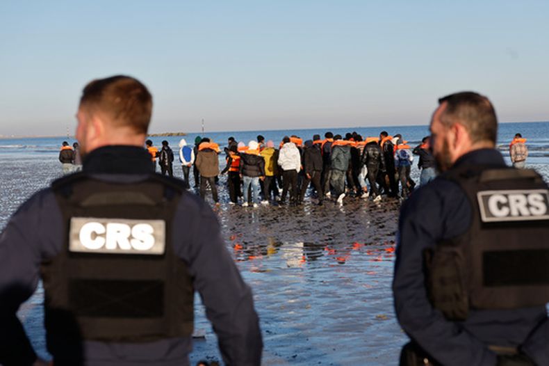 Policías miran a migrantes que querían abordar una lancha para llegar a Reino Unido, el miércoles 8 de abril de 2026 en Malo-les-Bains, en el norte de Francia. (AP Foto/Jean-Francois Badias)