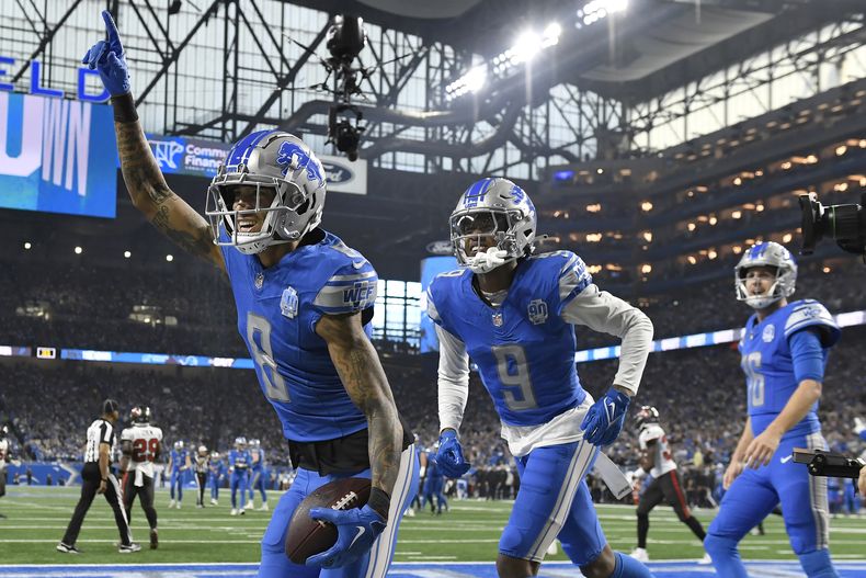 El wide receiver de los Lions de Detroit Josh Reynolds (8) celebra junto a sus compañeros Jameson Williams (9) y Jared Goff (16) luego de hacer un touchdown ante los Buccaneers de Tampa Bay durante la primera mitad del juego de ronda divisional en la postemporada de la NFL, el domingo 21 de enero de 2024, en Detroit. (AP Foto/Jose Juarez)
