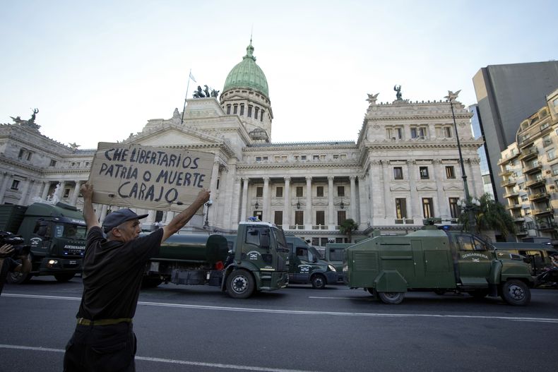 Un manifestante muestra un letrero de protesta ante la policía desplegada en las afueras del Congreso donde los legisladores debaten una reforma impulsada por el presidente argentino, Javier Milei, en Buenos Aires, Argentina, el jueves 1 de febrero de 2024. La propuesta incluye una amplia variedad de medidas económicas, administrativas, penales y medioambientales. (AP Foto/Natacha Pisarenko)