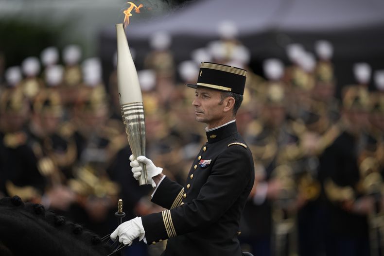 El coronel Thibault Vallette, del cuerpo de instructores de hípica Cadre Noir de Saumur, lleva la antorcha olímpica durante el desfile del Día de la Bastilla el domingo 14 de julio de 2024 en París. (AP Foto/Louise Delmotte)