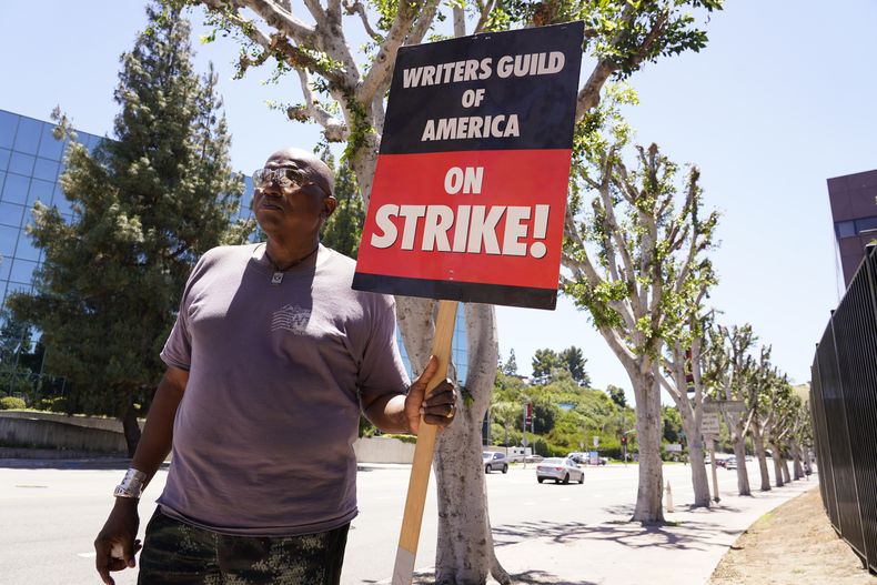 Dee Thompson, miembro del sindicato WGA y SAG-AFTRA, pasa junto a unos árboles árboles recién podados con un cartel en una manifestación frente a los estudios Universal el miércoles 19 de julio de 2023 en Burbank, California. (Foto AP/Chris Pizzello)