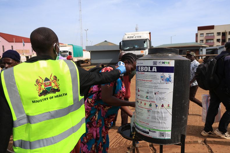 Varias personas se desinfectan las manos mientras un trabajador sanitario comprueba la temperatura de viajeros que cruzan de Uganda a Kenia, como parte de las medidas para contener la propagación del virus del ébola, en Busia, Kenia, el 15 de octubre de 2026. (AP Foto/Andrew Kasuku)