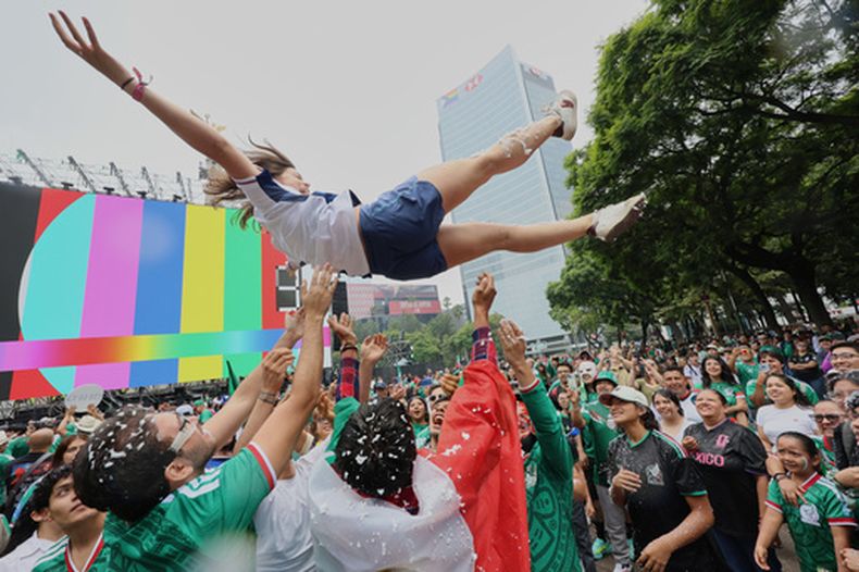 Aficionados al fútbol lanzan por los aires a una mujer, durnate una fiesta para mirar el partido de la selección de México ante Inglaterra, mediante una pantalla gigante instalada en la capital, el domingo 5 de junio de 2026 (AP Foto/Ginnette Riquelme)