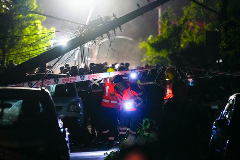 Los equipos de rescate caminan cerca de un poste de electricidad caído sobre un automóvil dañado por un tornado en Requinoa, Chile, el lunes 26 de octubre de 2026. (AP Foto/Esteban Félix)