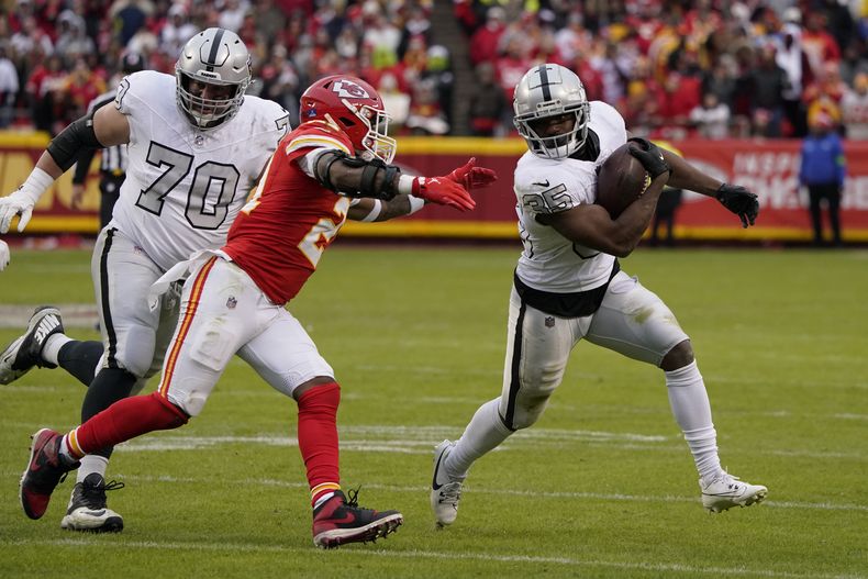 El corredor de los Raiders de Las Vegas Zamir White corre con el balón mientras lo persigue el safety de los Chiefs de Kansas City Mike Edwards y el guard de los Raiders Greg Van Roten observa el lunes 25 de diciembre del 2023. (AP Foto/Ed Zurga)