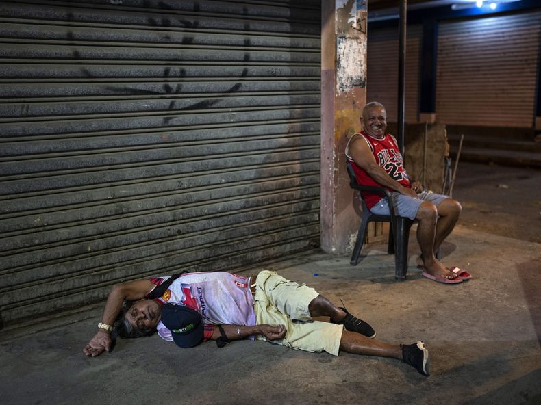Un hombre duerme borracho en una acera junto a un vendedor de cangrejos que espera clientes, en Durán, una ciudad ubicada frente a Guayaquil, Ecuador, el 27 de septiembre de 2023. (AP Foto/Rodrigo Abd)
