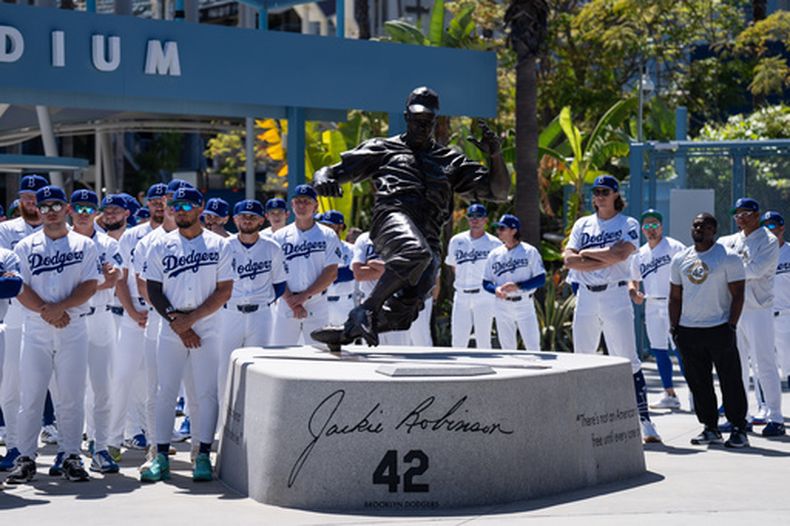 Miembros de los Dodgers de Los Ángeles se reúnen en torno de una estatua de Jackie Robinson antes de enfrentar a los Mets de Nueva York el miércoles 15 de abril de 2026 (AP Foto/Jae C. Hong)