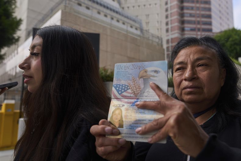 Margarita Velez, madre de Andrea Velez, de 32 años y ciudadana estadounidense residente en el sur de Estados Unidos, muestra el pasaporte de su hija junto a su hija menor, Estrella Rosas, de 17 años, a la izquierda, mientras intentan averiguar el paradero de Andrea después de que fuera detenida por agentes del ICE en una redada migratoria en el centro de la ciudad, ante el Centro Metropolitano de Detención en los Ángeles, el miécoles 25 de junio de 2025. (AP Foto/Damian Dovarganes)
