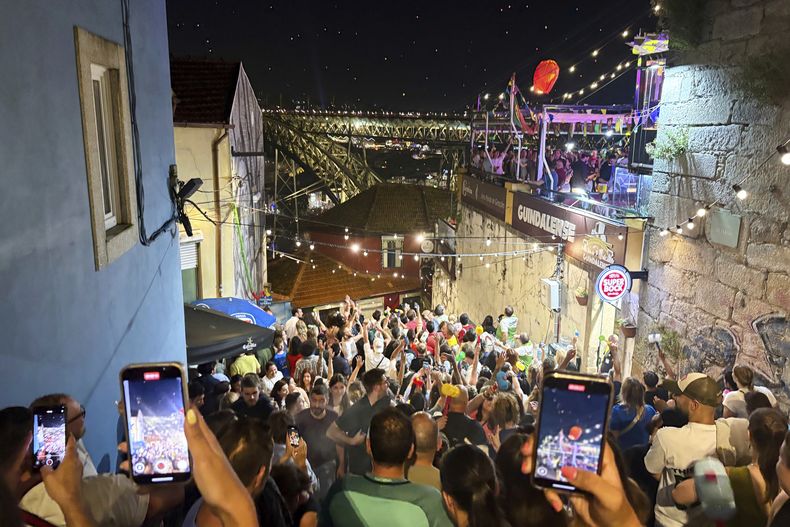 Gente celebra y graba videos mientras un grupo de personas lanza un farol al aire durante las celebraciones de la víspera de San Juan junto al río Duero, en Oporto, en el norte de Portugal, el lunes 23 de junio de 2025. (AP Foto/Helena Alves)