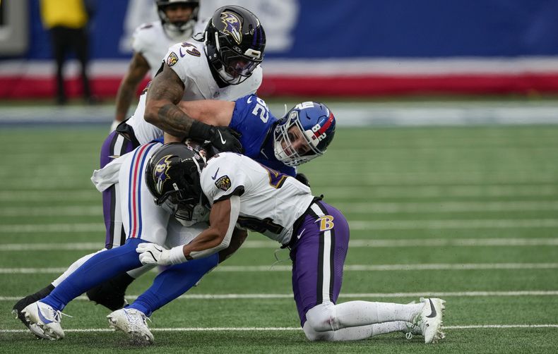 El linebacker Chris Board (49) y el cornerback Marlon Humphrey (44), de los Ravens de Baltimore, derriban al tight end Daniel Bellinger (82), de los Giants de Nueva York, durante el tercer cuarto del partido de la NFL del domingo 15 de diciembre de 2024, en East Rutherford, Nueva Jersey. (AP Foto/Seth Wenig)