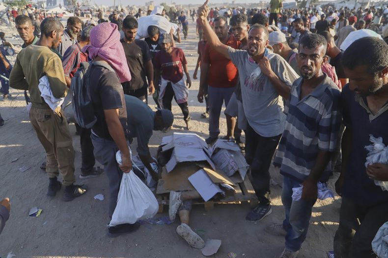Palestinos, junto al cuerpo de una mujer que fue golpeada por un camión cuando intentaba alcanzar un camión en un convoy de ayuda humanitaria que circulaba por el corredor de Morag, cerca de Rafah, en el extremo sur de la Ciudad de Gaza, el 4 de agosto de 2025. (AP Foto/Mariam Dagga)