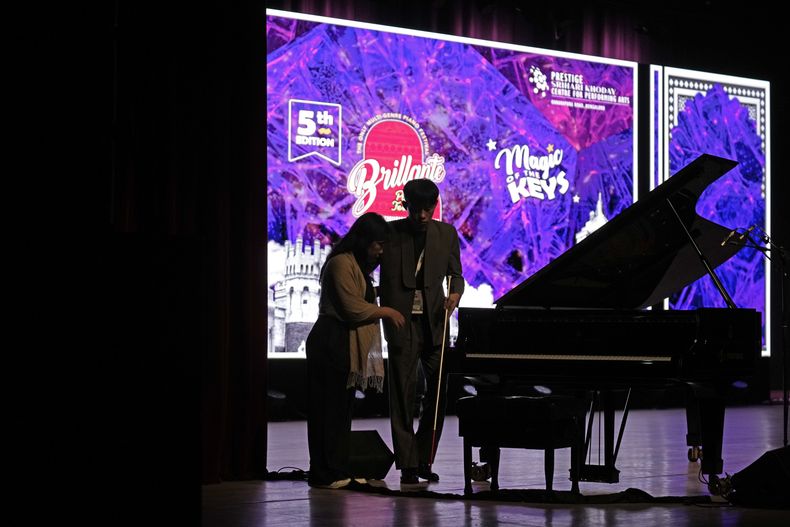 Imlibenla Jamir, de 30 años, a la izquierda, guía a su hermano Takosangba Pongen, de 27 años, un pianista ciego, al escenario para su actuación en el Festival de Piano Brillante de dos días en Bengaluru, India, el domingo 29 de septiembre de 2024. (Foto AP/Aijaz Rahi)