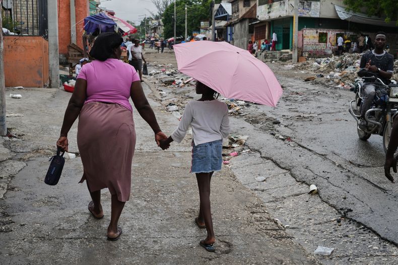 Una mujer camina de la mano con una niña con paraguas bajo una suave lluvia, el 23 de octubre de 2025, en Puerto Príncipe, Haití. (AP Foto/Odelyn Joseph)