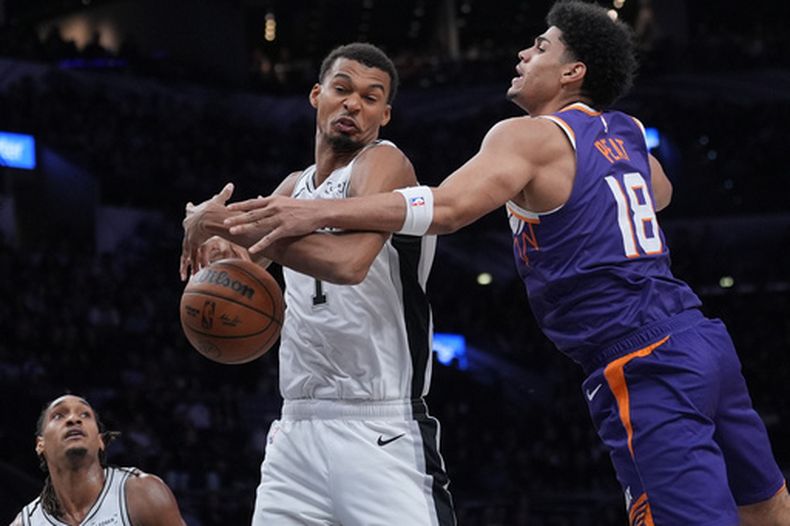 El delantero de los Spurs de San Antonio, Victor Wembanyama (1), y el delantero de los Suns de Phoenix, Koa Peat (18), disputan un rebote durante la primera mitad de un partido de básquetbol de pretemporada de la NBA en San Antonio, el miércoles 14 de octubre de 2026. (Foto AP/Eric Gay)