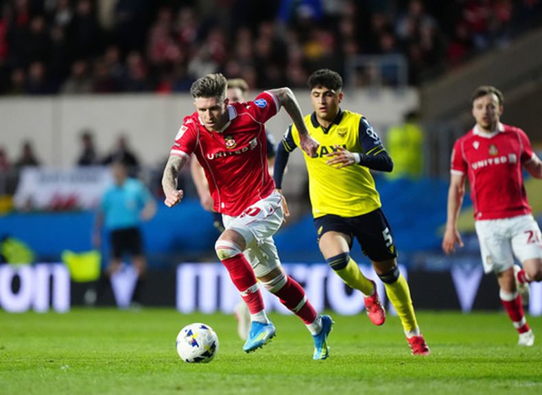 Josh Windass de Wrexham se desmarca de Yunus Konak de Oxford United para anotar un gol en el partido de la segunda división de Inglaterra, el martes 28 de abril de 2026, en Oxford, Inglaterra. (David Davies/PA vía AP)